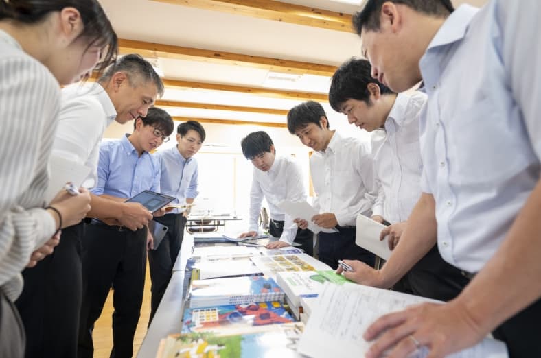 複数人の社員がテーブルに置かれた資料を見ながら話し合う様子